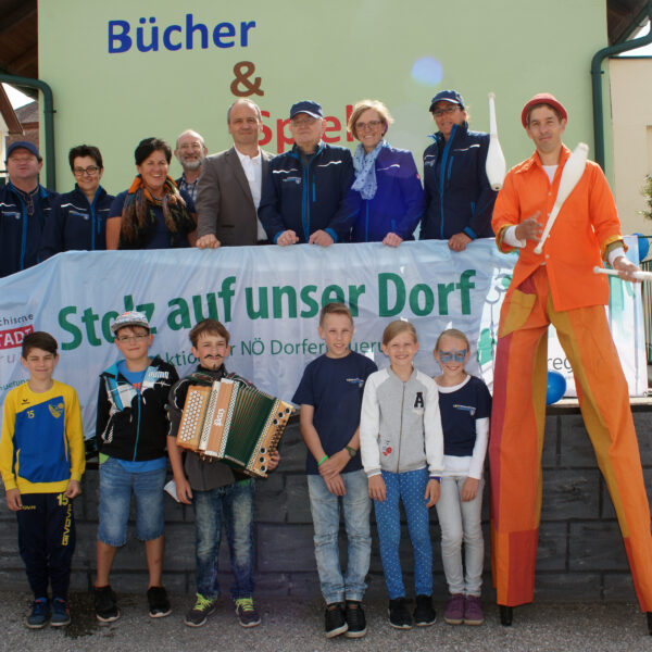 Kinder, Erwachsene und ein Stelzengeher in oranger kleidung bei der Eröffnung des Bücher- und Spielehauses in Wiesmath