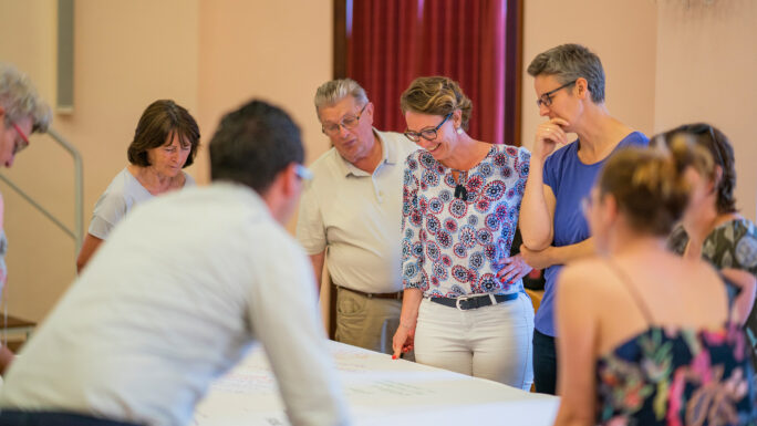 Menschen beugen sich über ein Plakat und besprechen ein Projekt.