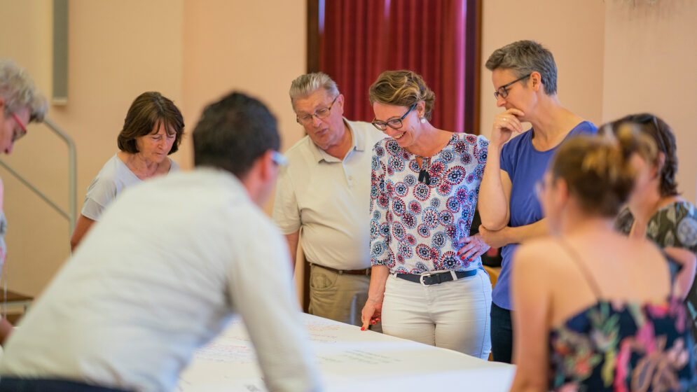 Menschen beugen sich über ein Plakat und besprechen ein Projekt.