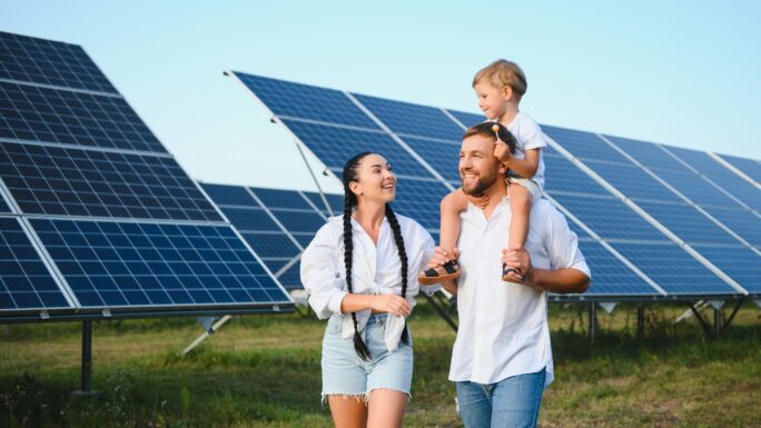 Begeisterter Vater zeigt das Potenzial alternativer Energie. Moderne Familie betrachtet die neue Solaranlage, die sie gekauft hat. Seitenansicht von glücklichen Eltern und interessiertem Kind neben den Solarpanels.