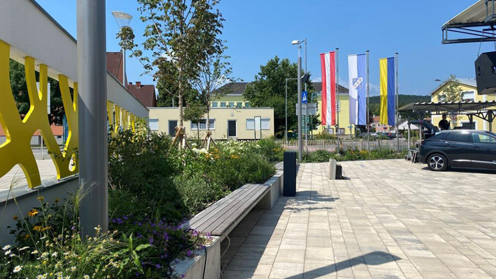 Das Foto zeigt den neugestalteten Rathausplatz in Enzesfeld-Lindabrunn mit Blick auf die vor dem Rathaus wehenden Fahnen.