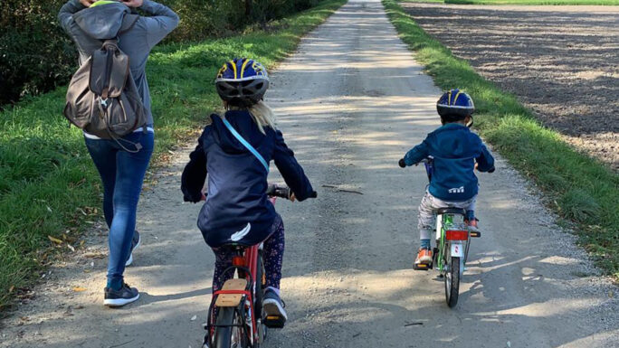 Das Bild zeigt eine Frau, die zu Fuß geht und zwei Kinder auf Fahrrädern von hinten am Weidner Rundweg.