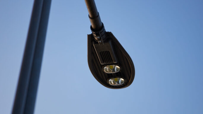Moderne Straßenbeleuchtung mit zwei LEDs auf schwarzem Mast, Stadtentwicklung, Stadtpark, blauer Himmel.