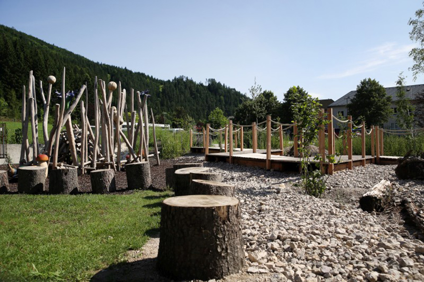 Das Bild zeigt den mit Holzsteg und Baumstammteilen als Motorik-Park gestalteten Bereich der Begegnungszone.