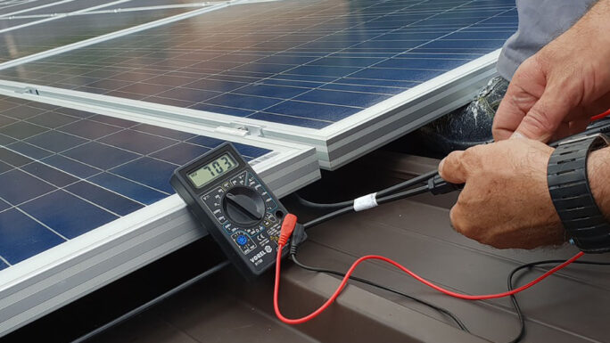 Männerhände, die mit einem Messgerät ein Solarpaneel überprüfen