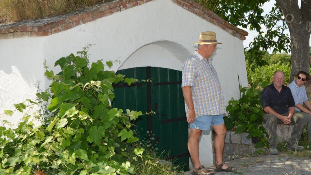 Ein Mann steht und ein Paar sitzt neben einem Eingang zu einem Weinviertler Weinkeller.