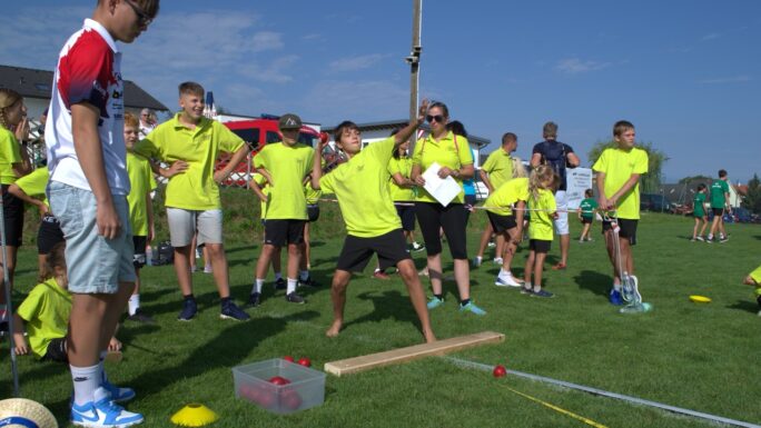 Kinder in verschiedenfarbigen Trikots messen sich im Weitwurf.