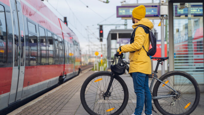Ein Mann in Winterkleidung steht am Bahnhof und ist dabei, mit seinem Fahrrad in den Zug einzusteigen.