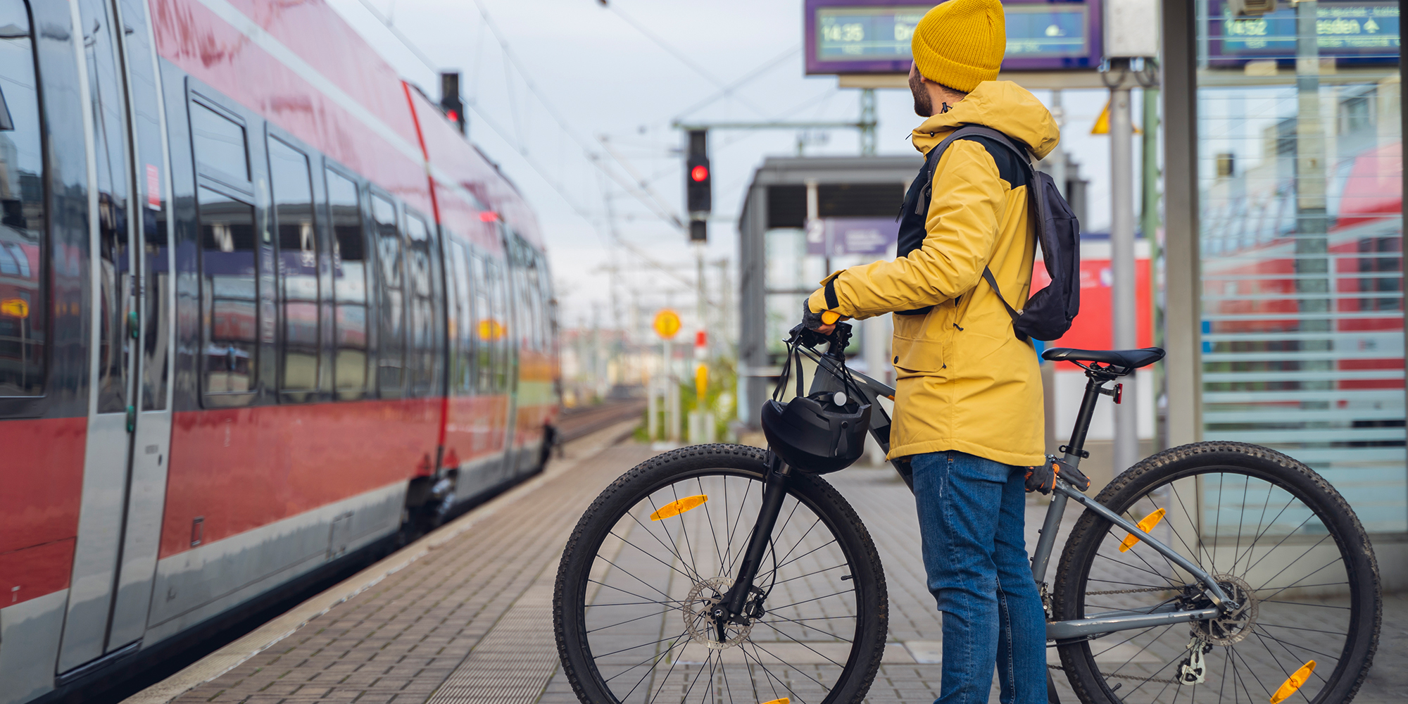 Ein Mann in Winterkleidung steht am Bahnhof und ist dabei, mit seinem Fahrrad in den Zug einzusteigen.