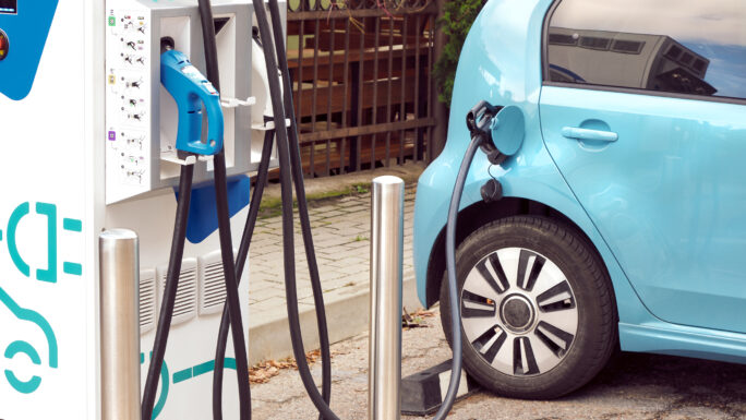 Ein Elektroauto an einer Ladestation auf der Straße, mit angeschlossenem Ladekabel.