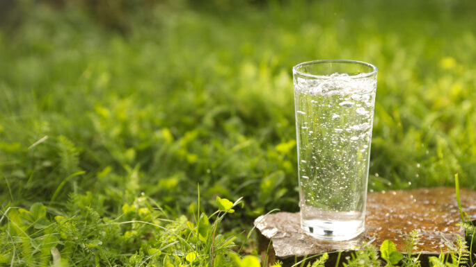ein Glas klares Wasser, dass auf einem Stein in einer grünen Wiese steht