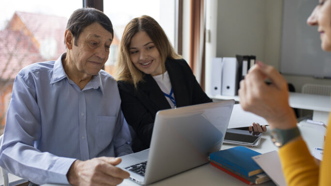 junge Frau erklärt älterem Mann den Umgang mit dem Laptop